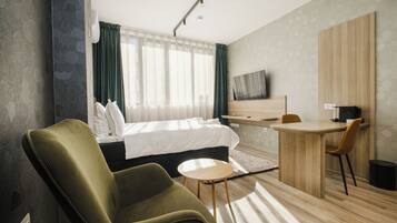 A modern hotel room with a bed, a desk, a chair, and a television.