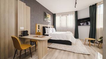 Una habitación de hotel moderna con una cama, un escritorio, dos sillas, una cafetera y un ventanal con cortinas.