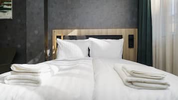 A neatly made bed with white linens and folded towels, a wooden headboard, and a textured wall behind.