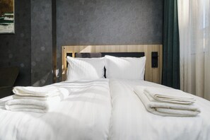 A neatly made bed with white linens and folded towels, a wooden headboard, and a textured wall behind. - A17 Suites (Plovdiv)