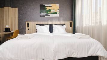 A hotel room with a large bed, a desk, a chair, and a painting on the wall.
