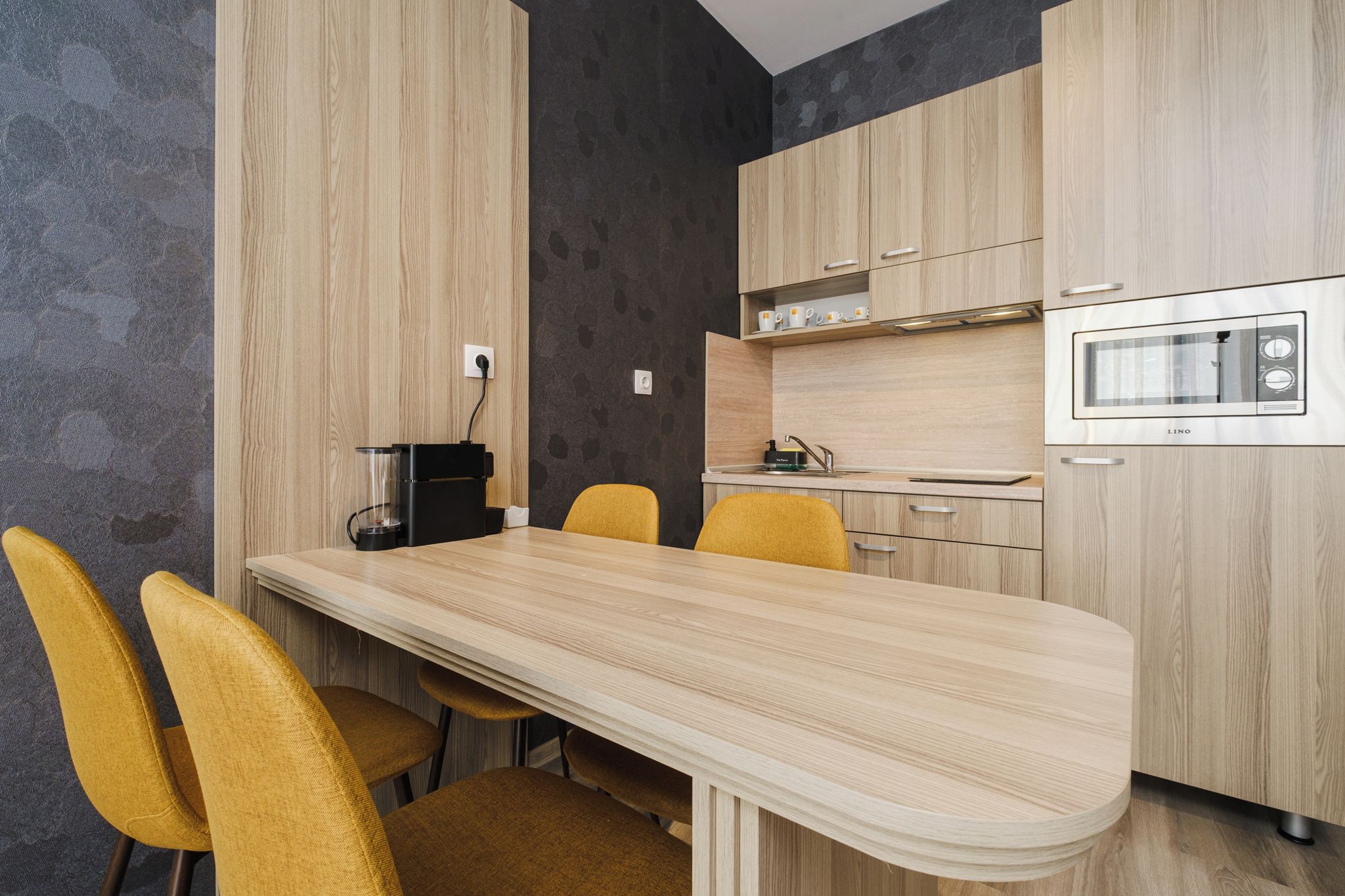 A modern kitchen with a wooden table and chairs, a built-in oven, and a coffee machine.