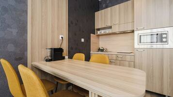 A modern kitchen with a wooden table and chairs, a built-in oven, and a coffee machine.