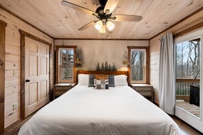 A bedroom with a large bed, wooden walls, a ceiling fan, and windows with curtains. - New listing discount! Pickleball- Hot Tub- Gameroom- 6 min to town: all 5-stars! (Blue Ridge)