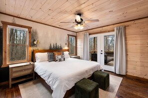 Ein Schlafzimmer einer Holzhütte mit Bett, Nachttischen, Deckenventilator und Blick ins Freie.