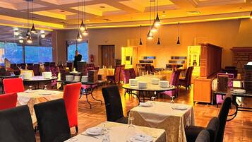 Un restaurante con varias mesas dispuestas para comer, iluminación colgante y vistas al exterior.
