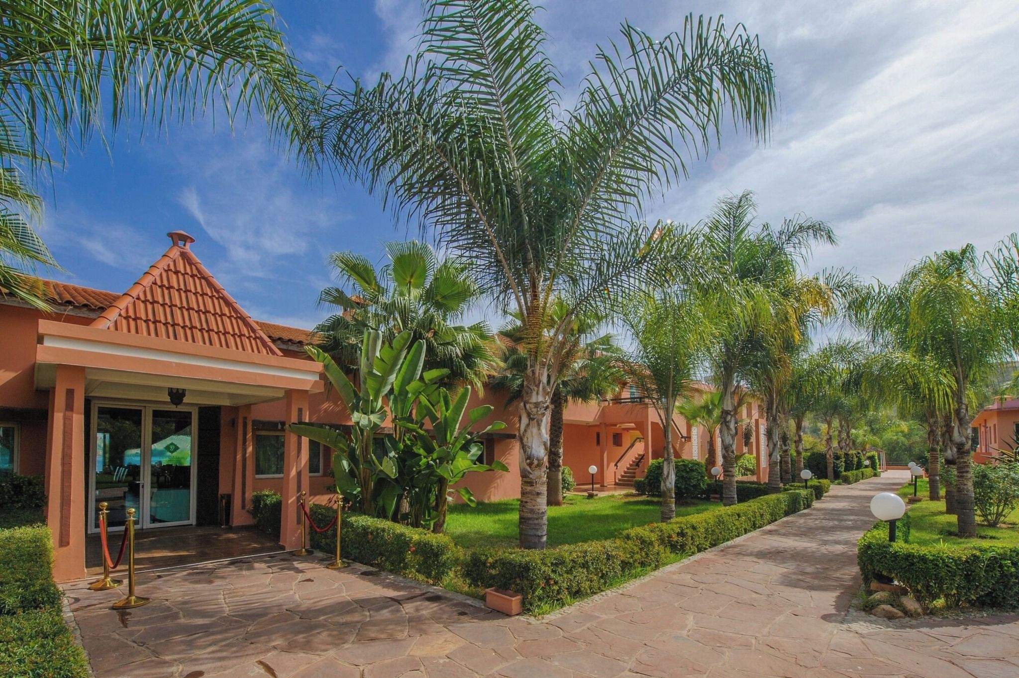 A resort with palm trees, a tiled roof, and a paved walkway.