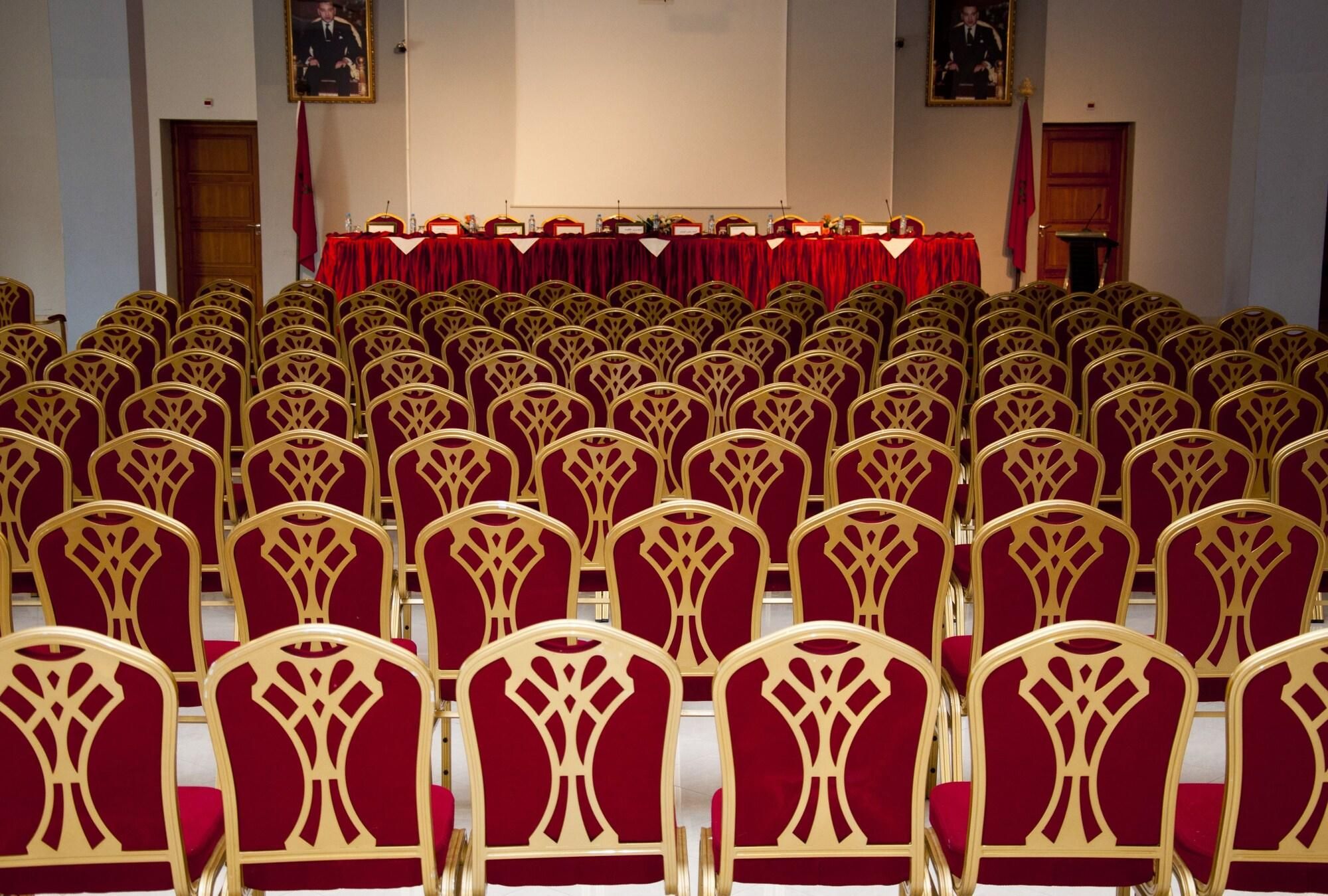 Des rangées de chaises, une table rouge et un pupitre dans une salle de conférence.