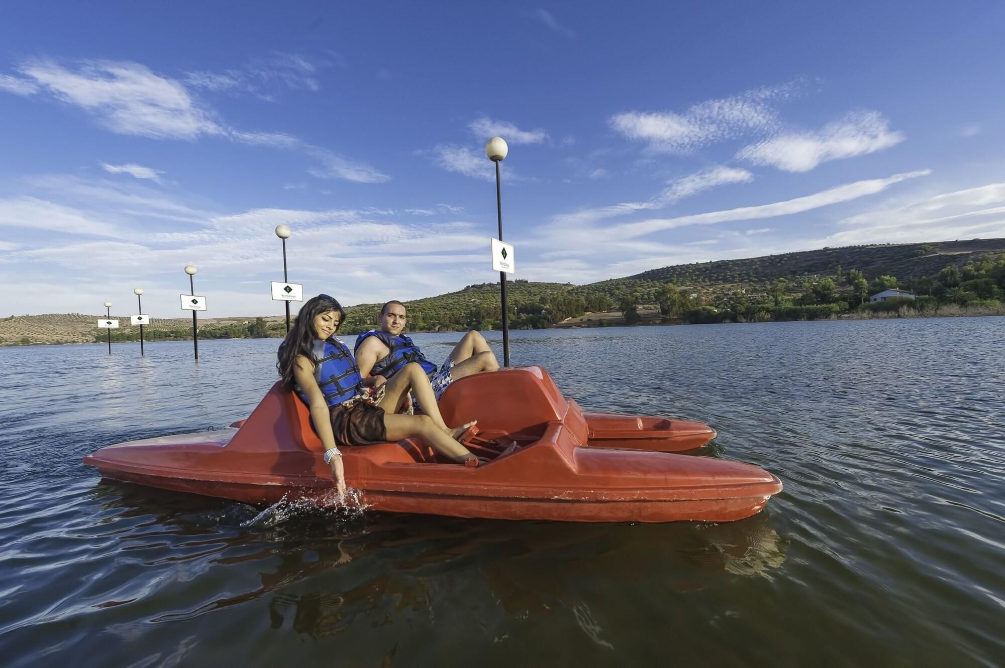 Un couple est assis sur un bateau rouge, avec un lac paisible et des collines en arrière-plan.