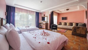 A hotel room with two beds, a sofa, a TV, and a desk.