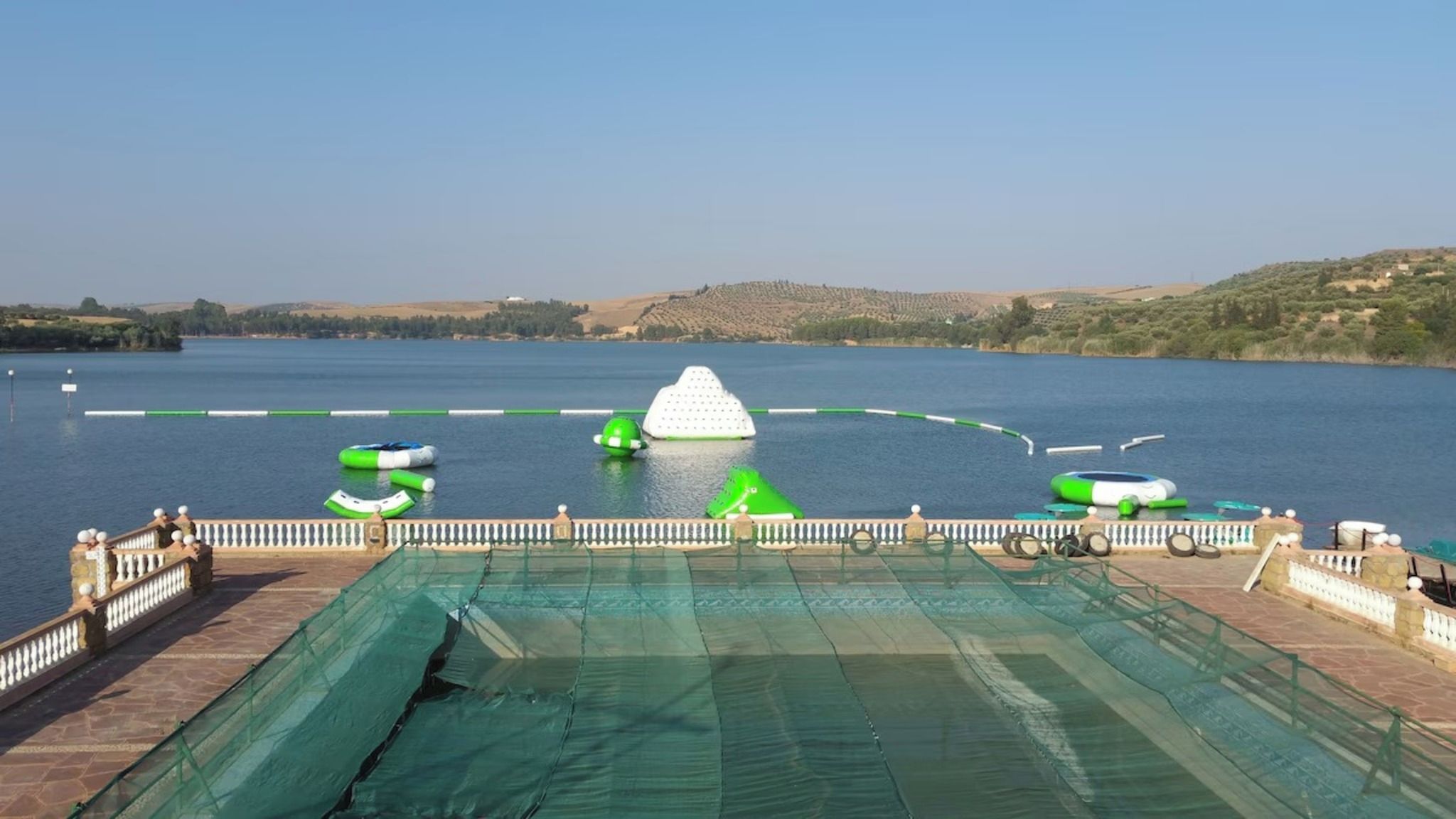 A waterfront view with a pool, inflatable toys, and a distant hill.