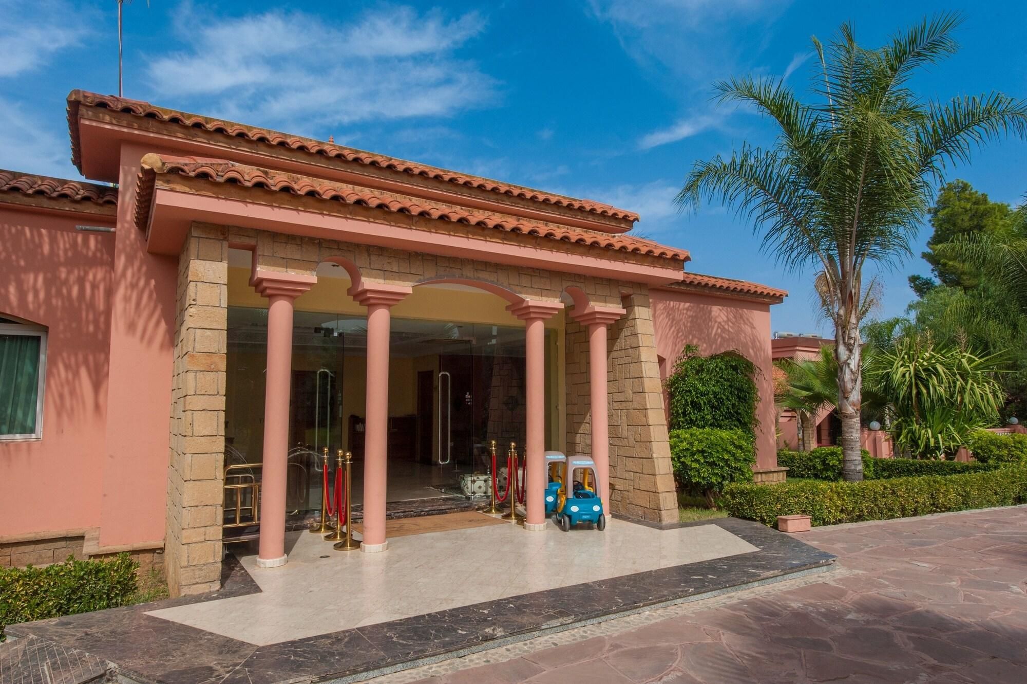 Un edificio con un vestíbulo cubierto, columnas y una palmera al fondo.