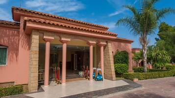 Un edificio con un vestíbulo cubierto, columnas y una palmera al fondo.