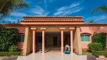 A building with a red-tiled roof, a central entrance with columns, and a small blue vehicle parked outside.