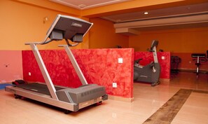 A fitness center with treadmills and a stationary bike, featuring a red wall and orange flooring.