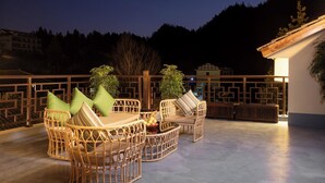 A rooftop terrace with wicker furniture, a small table with fruits, and a view of the surrounding landscape. - Zhangjiajie Valley Love Holiday Hotel (Zhangjiajie)