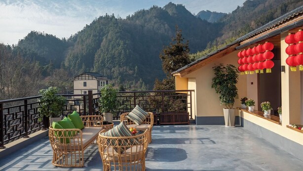 A terrace with wicker furniture, potted plants, and a view of mountains. - Zhangjiajie Valley Love Holiday Hotel (Zhangjiajie)