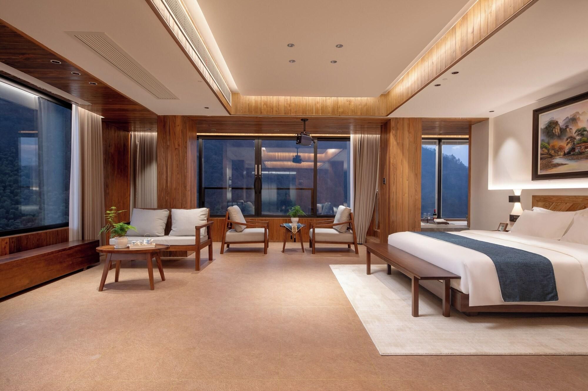 Ein modernes Hotelzimmer mit einem großen Bett, einer Sitzecke und großen Fenstern mit Blick.