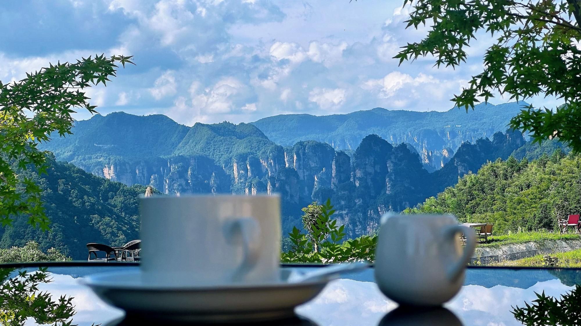 Una mesa con dos tazas y platillos blancos, con montañas y un cielo despejado de fondo.