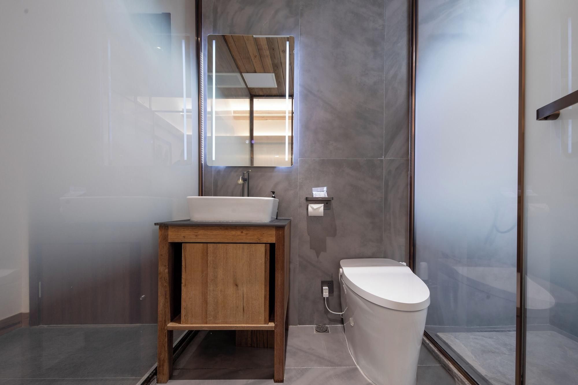 A modern bathroom with a wooden vanity, a white sink, a mirror, and a toilet.