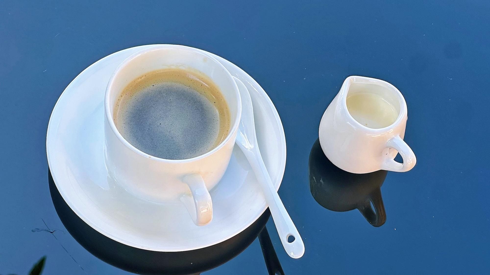 Une tasse de café posée sur une soucoupe, avec une cuillère, le tout placé sur une surface réfléchissante.