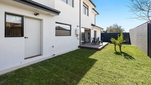 Et moderne hus med to etager, fladt tag, en lille forhave og en terrasse med udendørs møbler.