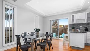 A modern kitchen with white cabinets, a granite countertop, and a dining area with a glass table and chairs. - Domi Rentals - The Lona Townhouse (Clayton)