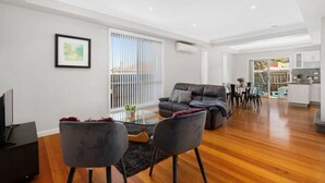 A modern living room with a sofa, chairs, a coffee table, and a TV. - Domi Rentals - The Lona Townhouse (Clayton)