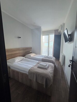 A hotel room with two beds, a television, and a window with curtains. - Hotel Corner (Batumi)