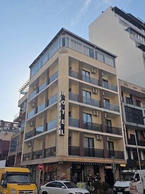 A multi-story hotel with balconies, a ground-level shop, and a visible sign for a restaurant. - Hotel Corner (Batumi)
