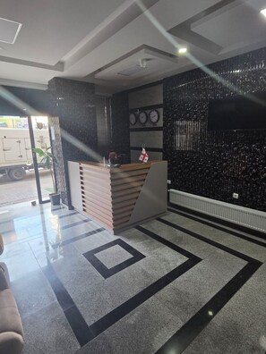 A reception area with a counter, a potted plant, and a wall with clocks. - Hotel Corner (Batumi)