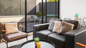 A modern living room with a sofa, chairs, a coffee table, and a large window. - Domi Rentals - The Balaclava Apartment (Caulfield North)