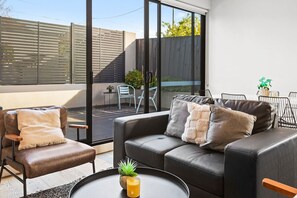 Ein modernes Wohnzimmer mit einer Couch, Sesseln, einem Couchtisch und einem großen Fenster.