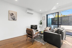 Ein modernes Wohnzimmer mit Sofa, Sesseln, Fernseher und Kunstwerken an der Wand.