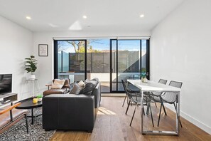 A modern living room with a sofa, TV, and dining area. - Domi Rentals - The Balaclava Apartment (Caulfield North)