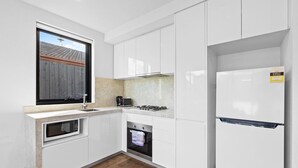 A modern kitchen with white cabinetry, a built-in oven, a microwave, a gas stove, and a refrigerator. - Domi Rentals - The Balaclava Apartment (Caulfield North)