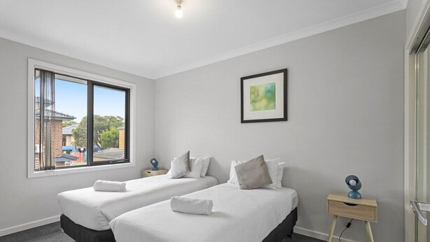 Ein Hotelzimmer mit zwei Betten, einem Fenster mit Aussicht, einem gerahmten Bild an der Wand und einem Nachttisch mit Lampe.