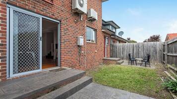 A brick house with a sliding glass door, a small patio with a table and chairs, and a wooden fence.