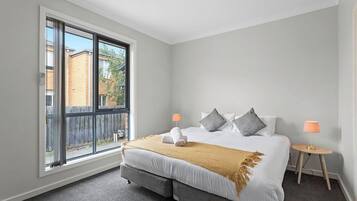 A bedroom with a large window, a bed with pillows, a bedside table, and a lamp.