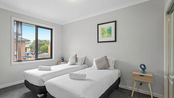A hotel room with two beds, a window with a view, a bedside table, and a wall-mounted picture.
