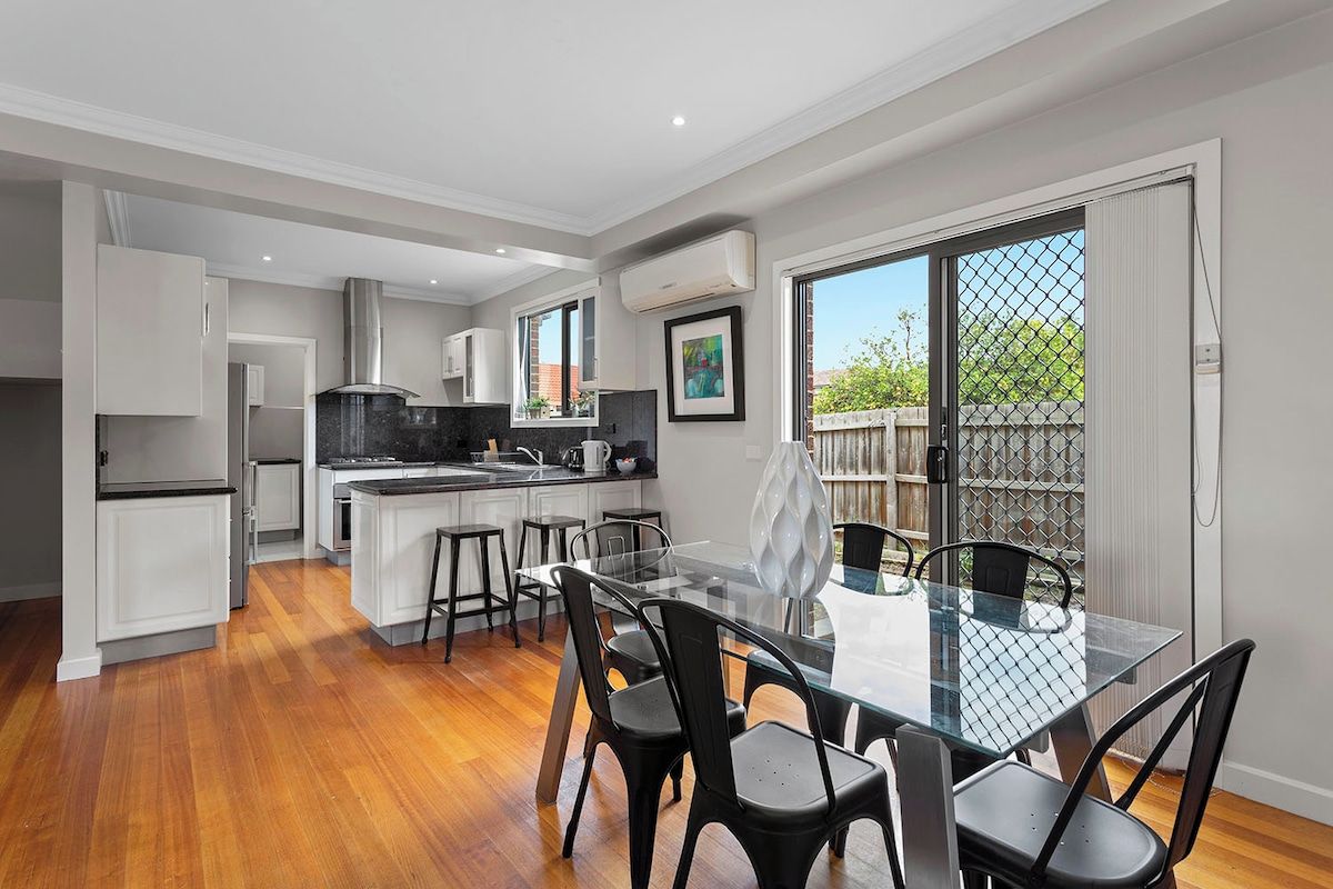 A modern kitchen with white cabinets, a black countertop, and a dining area with a glass table and black chairs.