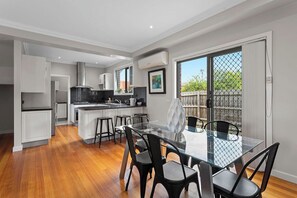A modern kitchen with white cabinets, a black countertop, and a dining area with a glass table and black chairs. - Domi Rentals - The Lantana Residence (Clayton)