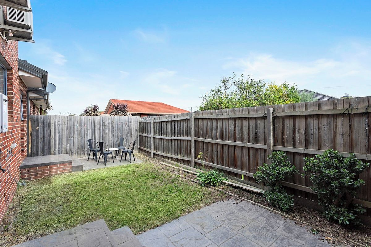 A backyard with a wooden fence, a patio with chairs, and a brick wall.