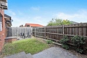 A backyard with a wooden fence, a patio with chairs, and a brick wall.