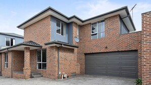 Ein zweistöckiges Ziegelhaus mit Garage, überdachter Veranda und kleinem Garten.