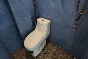 Un vàter blanc en un bany amb parets blaves i un terra emblenquinat.