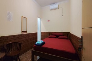 Una habitació petita amb un llit, una cadira, un mirall i una porta.