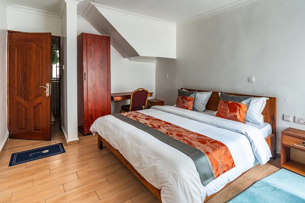 A hotel room with a large bed, a desk, and a wardrobe.