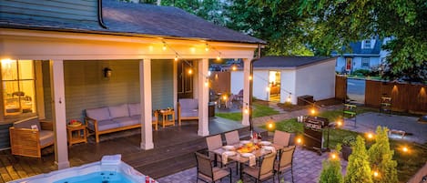 A covered outdoor patio with seating, a hot tub, and string lights.