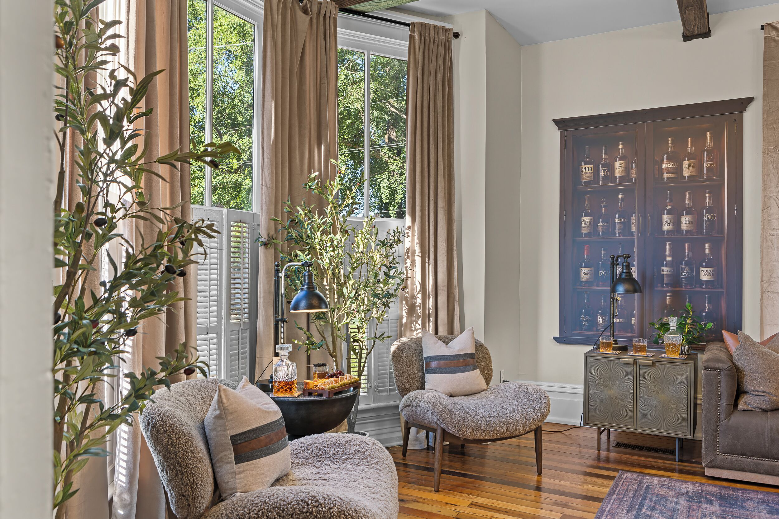 A cozy living room with a fireplace, comfortable seating, and a bookshelf with various bottles.